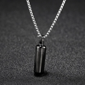 Detailed close-up of a black capsule pendant on a silver steel chain over a dark background