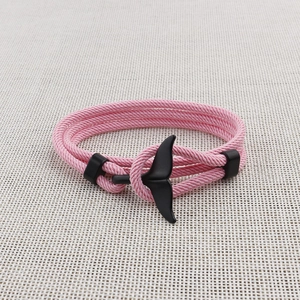 Close-up of a pink braided rope bracelet featuring a black metal whale tail charm