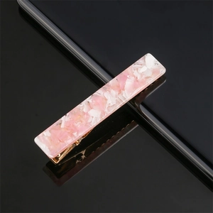 Macro shot of pink marble pattern acrylic hair clip with gold metal base on black reflective surface