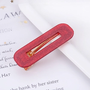 Close-up of red glitter acetate hair clip with gold metal base on white book