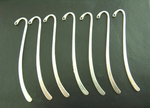 Detailed view of six curved silver-plated metal bookmarks with holes on a black surface