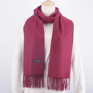 Close-up of wine red cashmere scarf with tassels and golden brand tag on white sweater