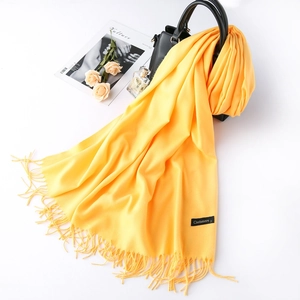 Solid yellow cashmere wool scarf with tassels draped over a black leather handbag