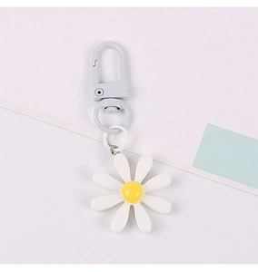 Detail view of a white daisy flower keychain with yellow center and blue metal clasp