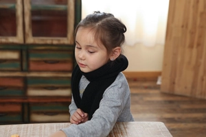 Close-up of a child wearing a black ribbed knit scarf in a warm home setting