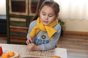 Detail shot of a yellow ribbed knit scarf for kids styled with a casual grey sweatshirt