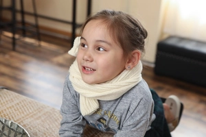 Detail of a child wearing a cream knit scarf and small heart earrings in soft light