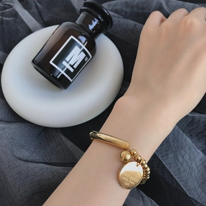 Minimalist gold titanium steel bead bracelet with engraved round pendant worn on wrist