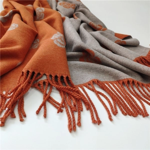 Close-up of double-sided cashmere-style scarf with orange camellia jacquard and tassels