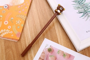 Close-up of a brown cartoon bear gel pen on a wooden desk with stationery props