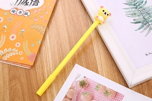 Close-up of a yellow cartoon pen with a 3D bear character on a wooden desk with stationery