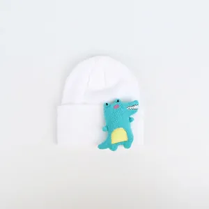 Detail der weißen Strickmütze mit einer süßen blauen Cartoon-Dinosaurier-Plüschfigur