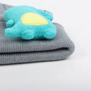 Detailed close-up of grey knitted beanie featuring a blue 3D cartoon dinosaur doll