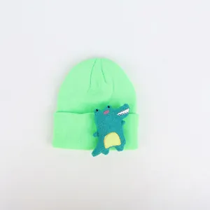 Detailaufnahme der Kinderstrickmütze mit einem grünen Plüsch-Dinosaurier-Aufnäher