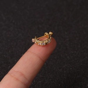 Macro shot of a small gold-plated helix piercing with sparkling zircons held on a fingertip