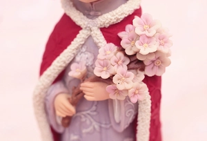 Macro detail of hand-painted resin figurine holding pink cherry blossom flower