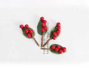 Dettaglio di quattro steli di bacche rosse artificiali con foglie verdi per decorazione