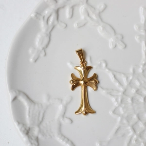Macro shot of 18K gold plated cross pendant on white ceramic dish with relief detail