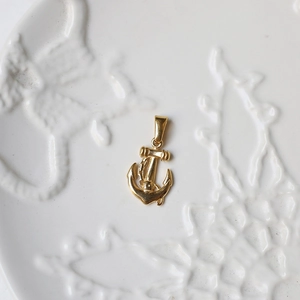Macro shot of 18K gold-plated anchor pendant on decorative ceramic tray detail