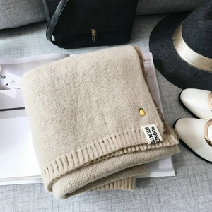 Détail d'une écharpe en maille beige et marron avec broderie ananas et étiquette