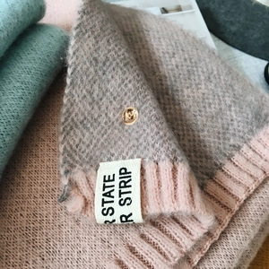 Détail d'une écharpe en maille rose et grise avec bouton-pression doré et étiquette en tissu
