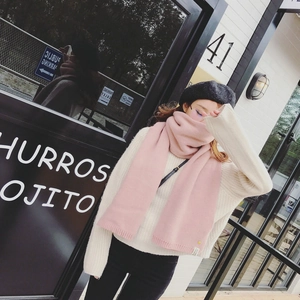 Détail d'une écharpe en tricot rose avec étiquette tissée et un pull de couleur crème
