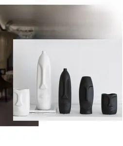 Close-up of five matte ceramic vases with abstract facial reliefs in black and white