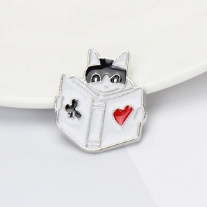 Macro detail of enamel cat brooch peering over a book with clover and heart patterns