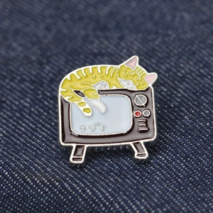 Detail of yellow enamel cat pin on vintage TV with Japanese text on denim jacket