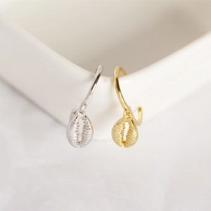 Detailed close-up of cowrie shell drop earrings in gold and silver finish on white ceramic