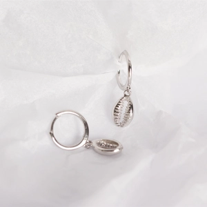 Macro shot of silver S925 huggie hoop earrings with delicate shell pendants on white fabric