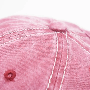Close-up of contrast white stitching and washed cotton texture on a rose pink baseball cap