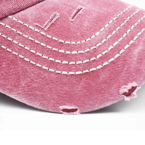Macro shot of washed pink denim baseball cap showing distressed details and white stitching