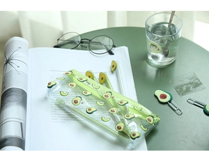 Flat lay of cute avocado stationery set with clear pencil case, pens, and ruler on magazine