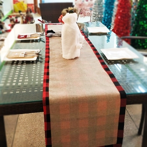 Close-up of rustic burlap Christmas table runner with red and black plaid borders on table