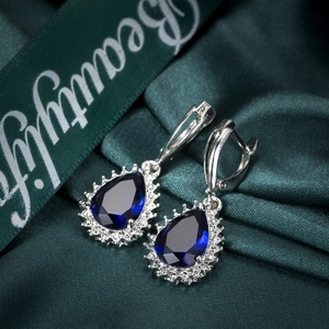 Macro view of blue pear-cut zircon drop earrings with silver pave settings on silk