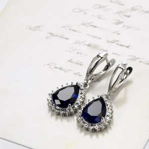 Detailed close-up of halo set pear cut blue sapphire earrings with silver leverback