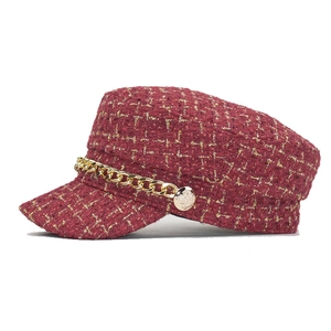 Close-up of wine red tweed beret with gold thread texture and metallic chain detail