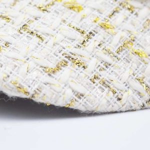 Close-up of white tweed fabric with metallic gold thread on a stylish wool beret hat