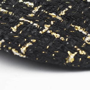 Macro shot of black tweed fabric featuring gold metallic threads and white woven patterns