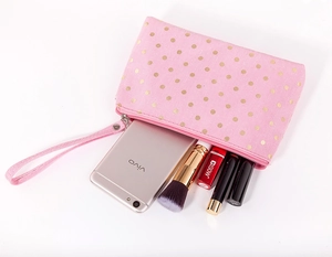 Detailed view of pink canvas makeup bag with gold polka dots holding cosmetics and phone