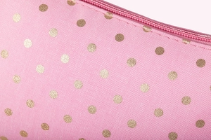 Macro shot of pink fabric texture with golden polka dots and zipper detail on the makeup bag
