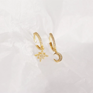 Macro shot of asymmetric gold star and moon drop earrings with sparkling crystals