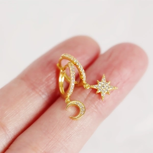 Gold asymmetric star and moon earrings with pave zircon crystals shown on a fingertip