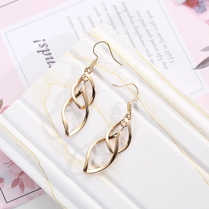 Detailed view of gold leaf twisted dangle earrings on a white marble background