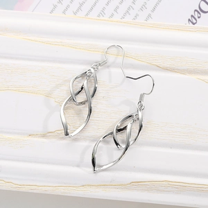 Detailed view of silver double-layered twisted geometric earrings on white wooden stand