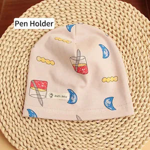 Detail of soft cotton baby beanie with moon and pencil print on natural mat