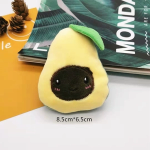 Detail shot of a plush avocado brooch accessory on a white surface with size labels