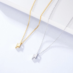Macro detail of minimalist gold and silver lightning bolt pendants on fine chain necklaces