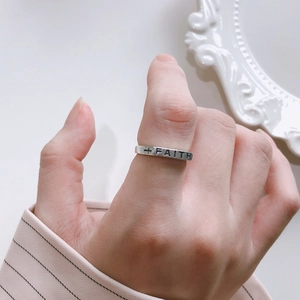 Close-up of minimalist silver faith cross ring worn on finger with pink striped cuff